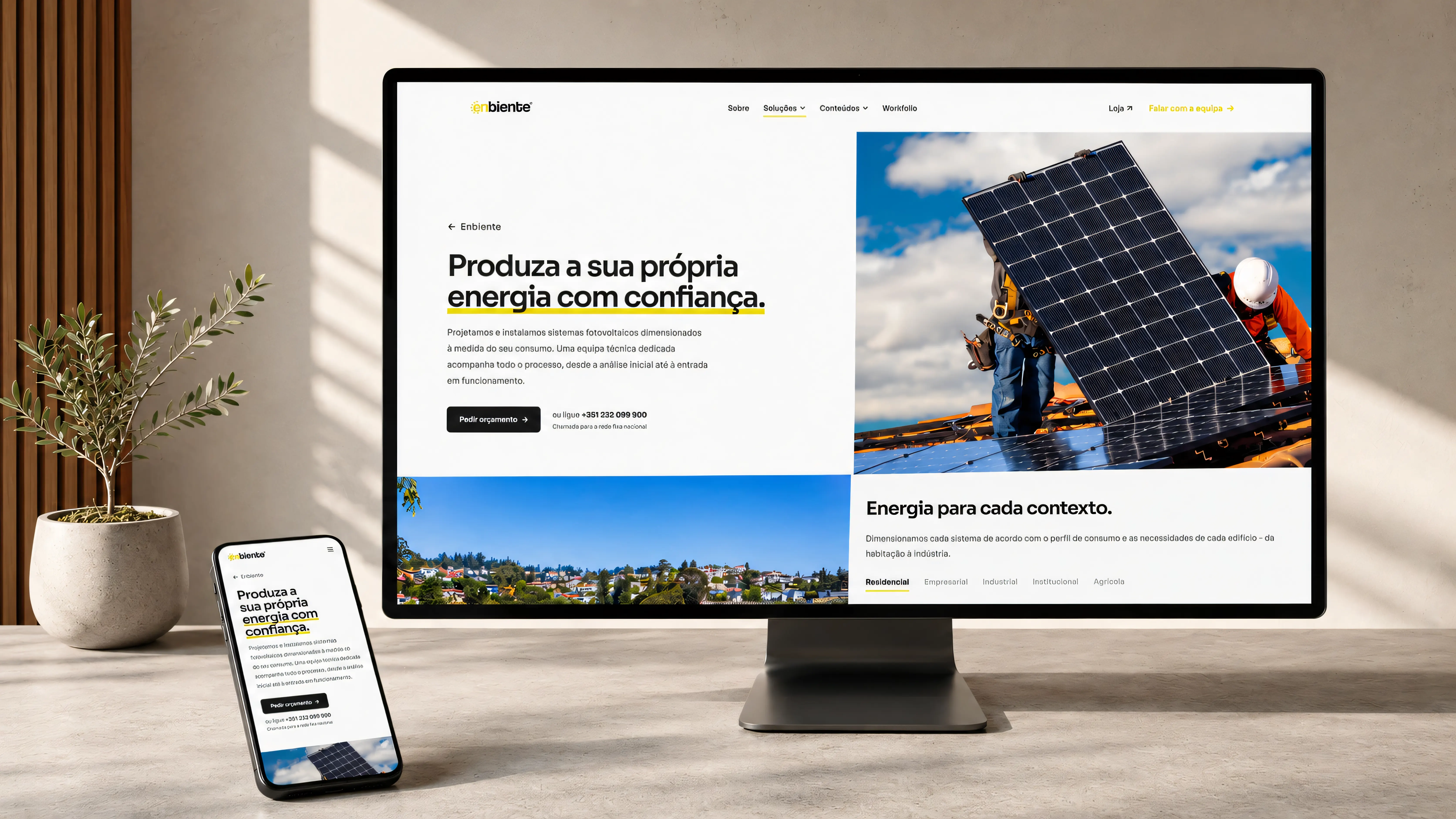 A página inicial do site reconstruído da Enbiente, num monitor e num telemóvel sobre uma secretária: título «Produza a sua própria energia com confiança», fotografia de instaladores a montar painéis solares e o menu de navegação.